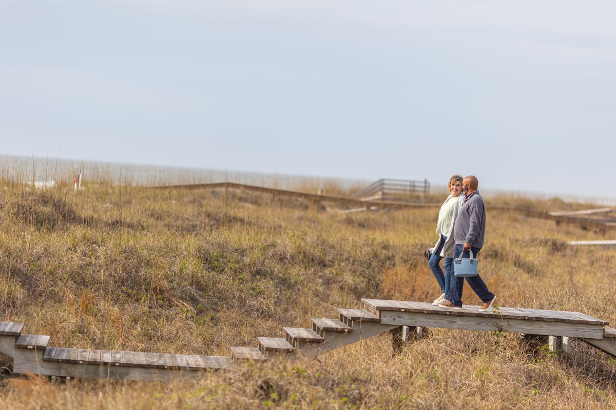 Couple walking a boardwalk through coastal dunes